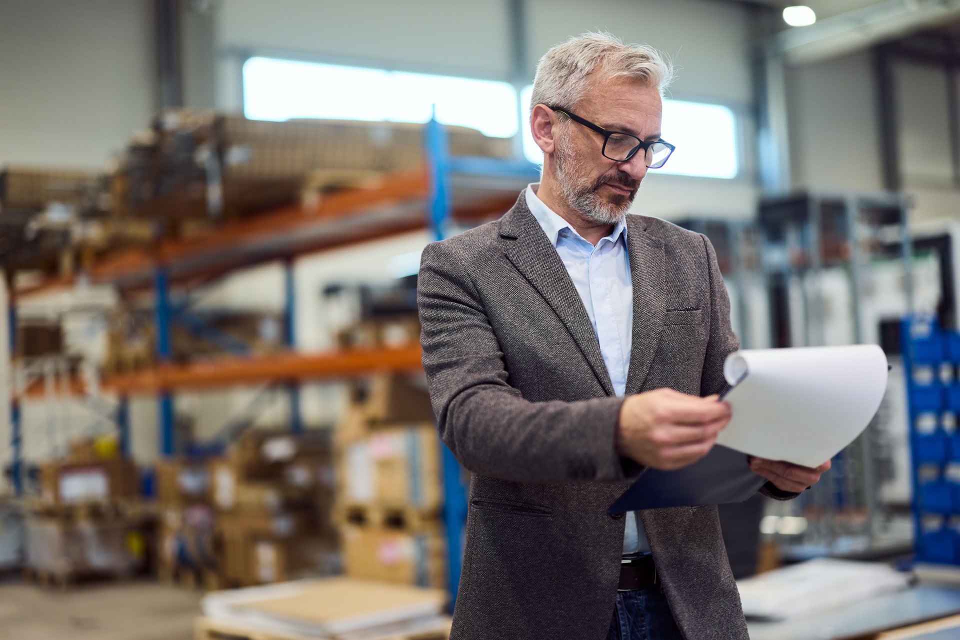 Professional Male Business Manager Evaluating Documents in a Large Industrial Warehouse